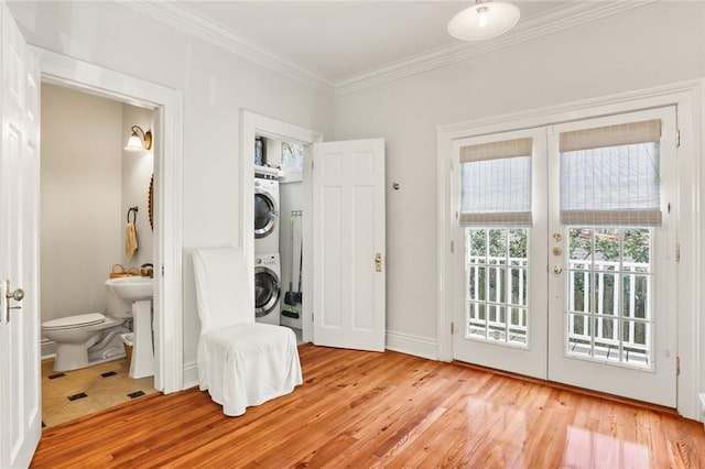 clothes washing area with stacked washer / dryer, light hardwood / wood-style flooring, french doors, and ornamental molding