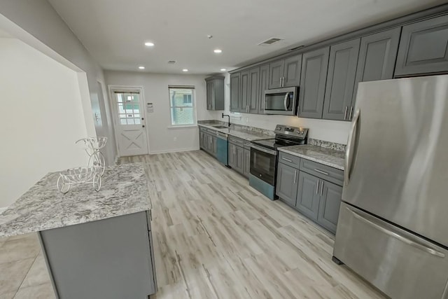 kitchen with sink, stainless steel appliances, gray cabinetry, and light hardwood / wood-style floors