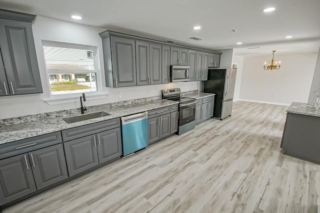 kitchen with appliances with stainless steel finishes, gray cabinetry, sink, a chandelier, and light hardwood / wood-style floors