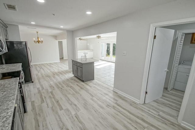 kitchen featuring light stone countertops, hanging light fixtures, light hardwood / wood-style flooring, gray cabinets, and ceiling fan with notable chandelier