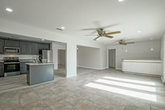 kitchen featuring light stone countertops, gray cabinetry, stainless steel appliances, a kitchen island with sink, and ceiling fan