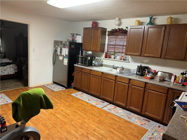 kitchen with appliances with stainless steel finishes, a textured ceiling, light hardwood / wood-style flooring, and sink