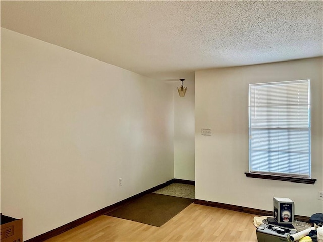 spare room with a textured ceiling, wood finished floors, and baseboards