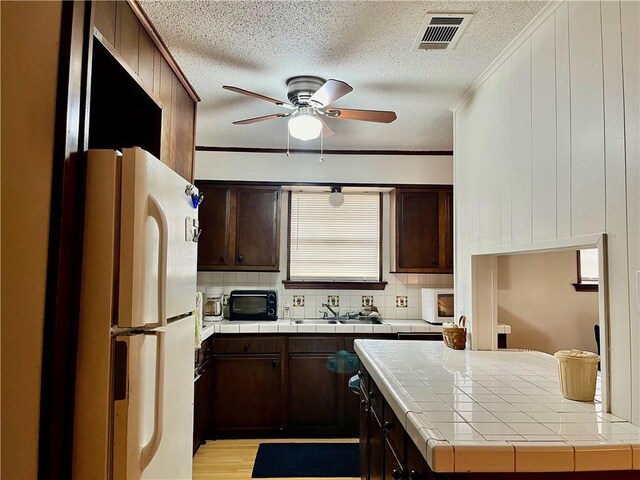 kitchen featuring white appliances, ceiling fan, tile countertops, dark brown cabinetry, and sink