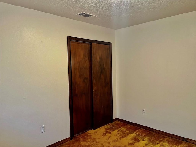 unfurnished bedroom featuring baseboards, visible vents, a textured ceiling, and carpet flooring