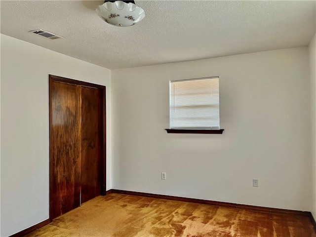 unfurnished bedroom featuring carpet floors, a closet, visible vents, a textured ceiling, and baseboards