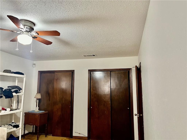 bedroom featuring ceiling fan, a textured ceiling, visible vents, and multiple closets