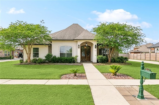 view of front facade with a front yard, roof with shingles, stucco siding, and fence