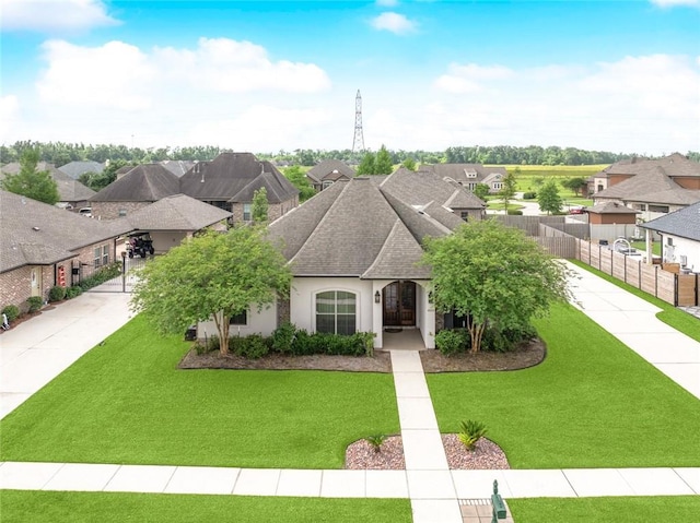 french country style house with a front lawn, a residential view, roof with shingles, stucco siding, and fence