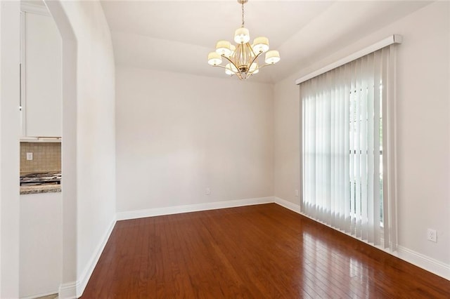empty room featuring arched walkways, an inviting chandelier, hardwood / wood-style flooring, and baseboards