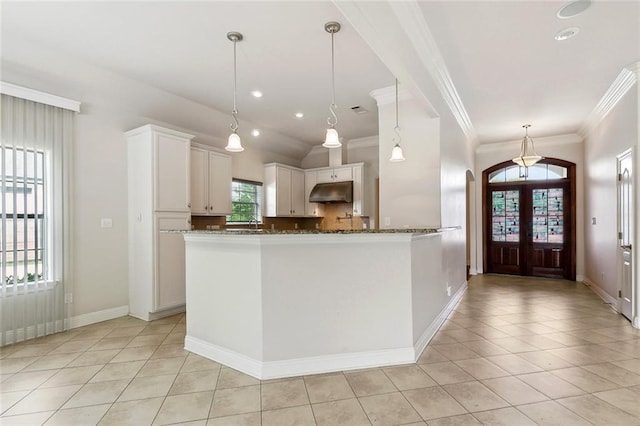 kitchen with dark stone countertops, light tile patterned floors, under cabinet range hood, white cabinets, and ornamental molding
