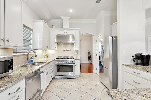 kitchen with light tile patterned floors, a sink, appliances with stainless steel finishes, under cabinet range hood, and ornamental molding