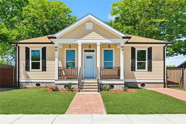 bungalow-style home featuring roof with shingles, a porch, a front lawn, and fence