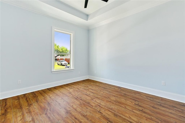 empty room featuring a ceiling fan, a raised ceiling, baseboards, and wood finished floors