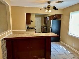 kitchen featuring light tile patterned floors, tile counters, a wealth of natural light, and stainless steel refrigerator