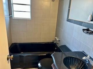 bathroom featuring toilet, tiled shower / bath, and tile walls