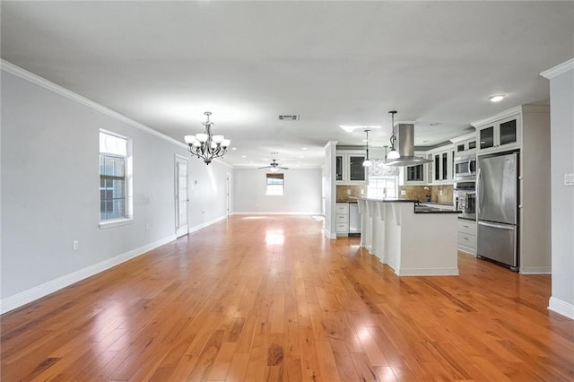 kitchen featuring island exhaust hood, white cabinetry, hanging light fixtures, and stainless steel appliances