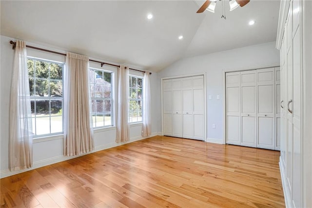 unfurnished bedroom featuring two closets, ceiling fan, lofted ceiling, and light wood-type flooring