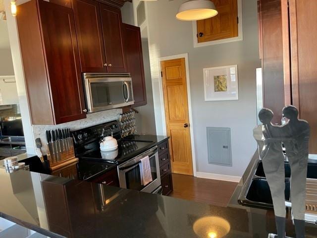 kitchen with electric panel, dark hardwood / wood-style flooring, backsplash, and appliances with stainless steel finishes