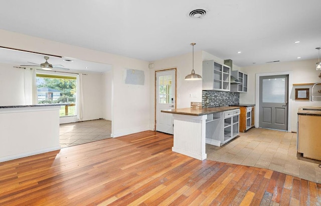 kitchen featuring kitchen peninsula, pendant lighting, light wood-type flooring, and backsplash