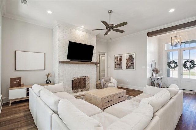 living room with ceiling fan with notable chandelier, ornamental molding, dark hardwood / wood-style floors, and a brick fireplace