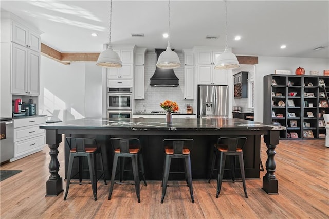 kitchen featuring pendant lighting, a breakfast bar area, appliances with stainless steel finishes, white cabinetry, and a spacious island