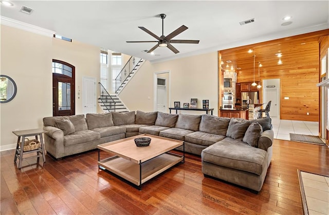 living room featuring ceiling fan, wood walls, ornamental molding, and dark wood-type flooring