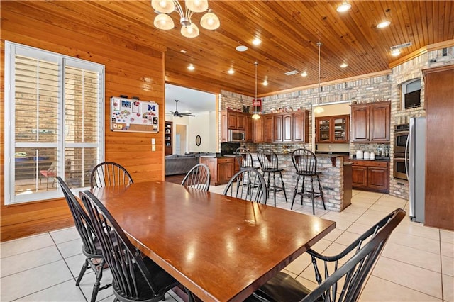 tiled dining room featuring ceiling fan with notable chandelier, wooden ceiling, and brick wall