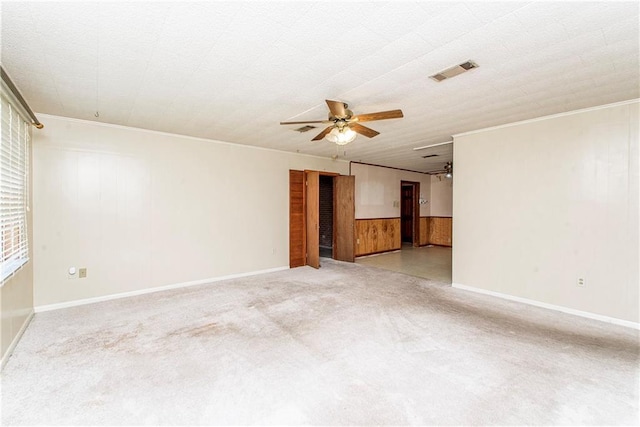 carpeted empty room featuring crown molding, visible vents, wood walls, and ceiling fan