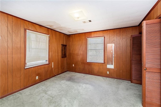 carpeted spare room featuring visible vents, baseboards, and wooden walls