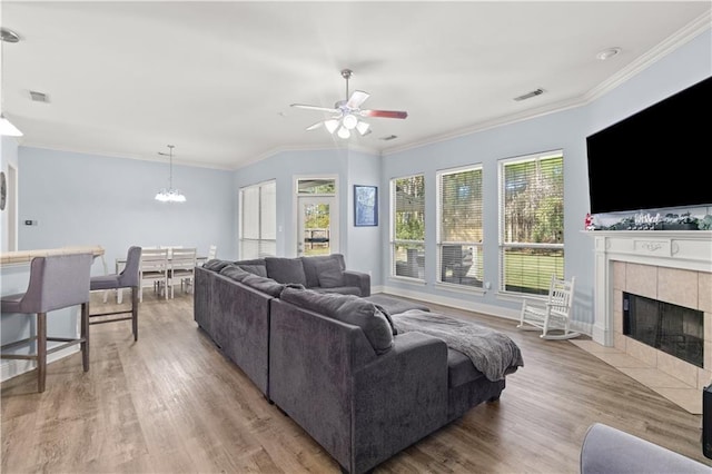 living room with ceiling fan with notable chandelier, light hardwood / wood-style floors, crown molding, and a tiled fireplace