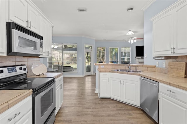 kitchen featuring white cabinets, tile counters, stainless steel appliances, and hanging light fixtures