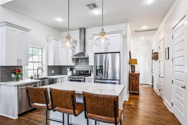 kitchen featuring appliances with stainless steel finishes, sink, wall chimney range hood, a kitchen island, and hanging light fixtures