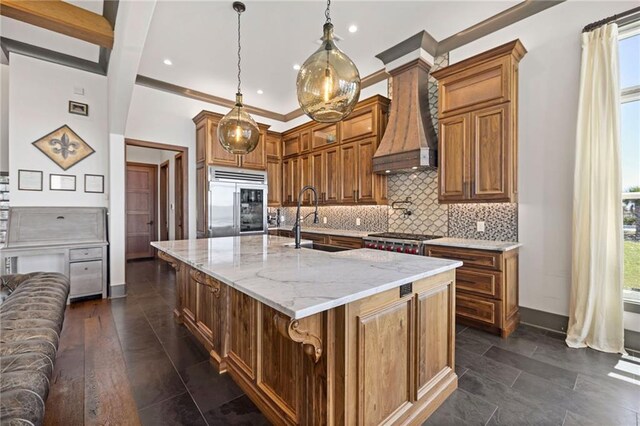 kitchen featuring decorative light fixtures, sink, a kitchen island with sink, built in refrigerator, and light stone counters