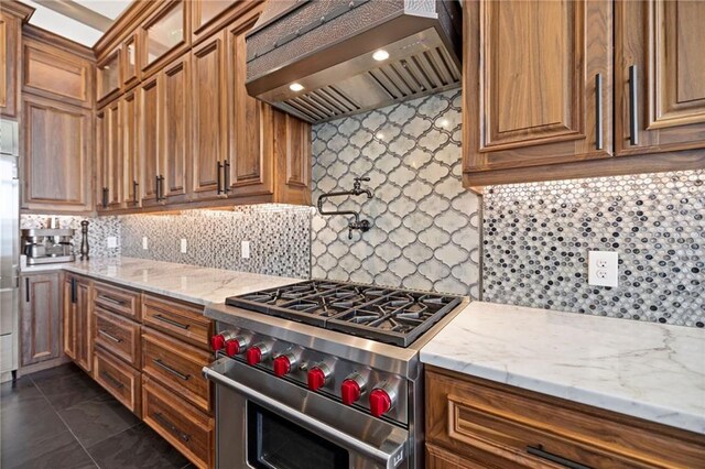 kitchen featuring high end range, custom exhaust hood, decorative backsplash, dark tile patterned floors, and light stone countertops