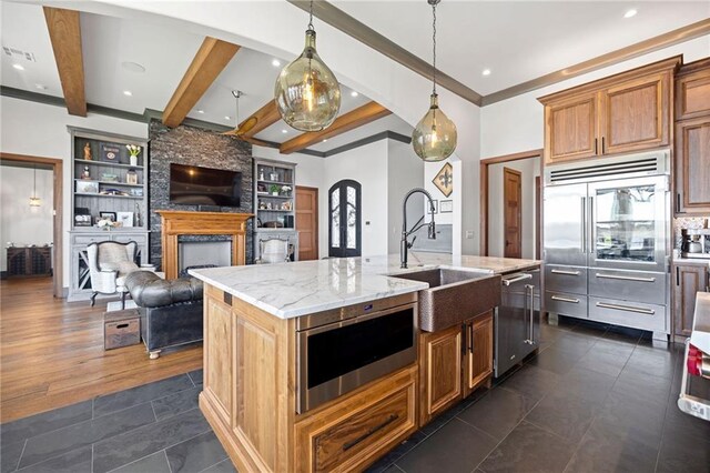 kitchen featuring a center island with sink, stainless steel appliances, decorative light fixtures, light stone countertops, and sink