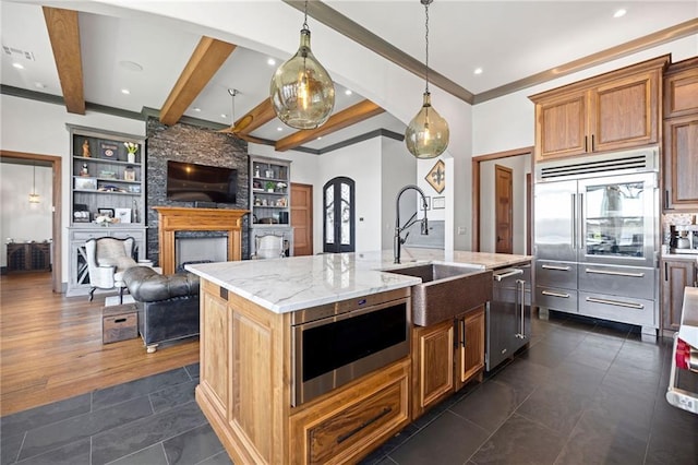 kitchen featuring appliances with stainless steel finishes, pendant lighting, an island with sink, sink, and light stone counters