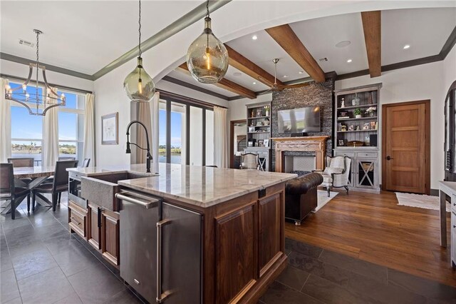 kitchen featuring light stone countertops, hanging light fixtures, a center island with sink, and beamed ceiling