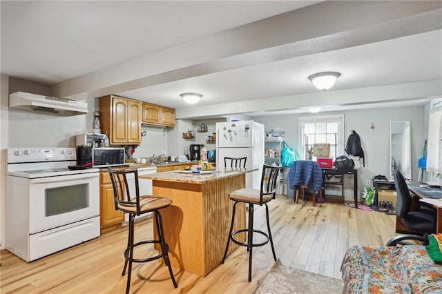 kitchen featuring a kitchen bar, range hood, light hardwood / wood-style floors, and white appliances