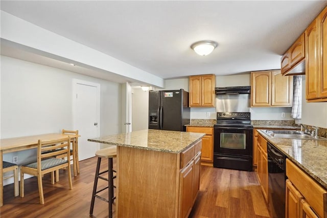 kitchen with black appliances, sink, dark hardwood / wood-style floors, a kitchen island, and light stone counters