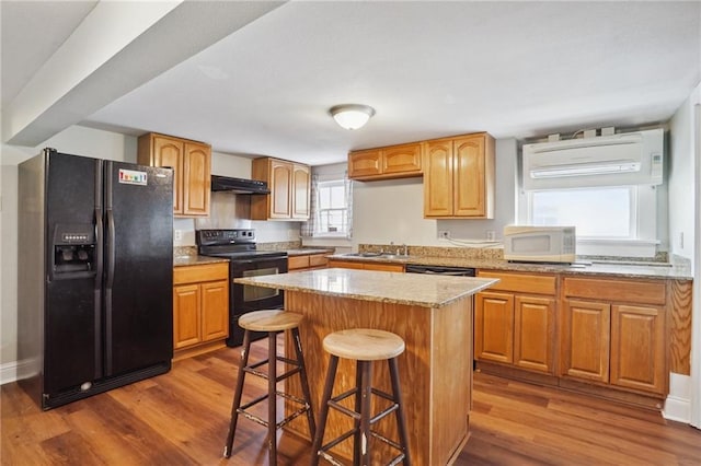 kitchen with a kitchen bar, dark hardwood / wood-style flooring, sink, black appliances, and a center island