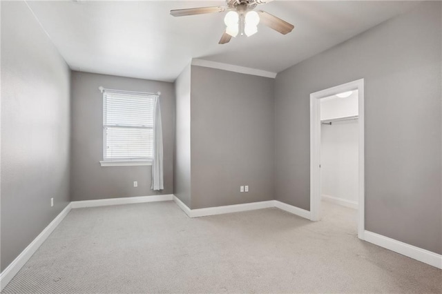 unfurnished bedroom with a closet, a walk in closet, light colored carpet, and ceiling fan