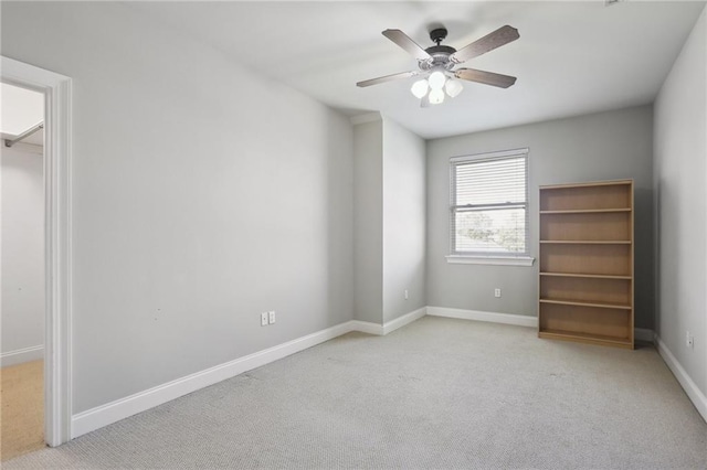 unfurnished bedroom featuring a walk in closet, ceiling fan, and light colored carpet