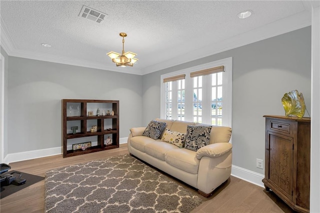 living room with hardwood / wood-style floors, ornamental molding, a textured ceiling, and an inviting chandelier