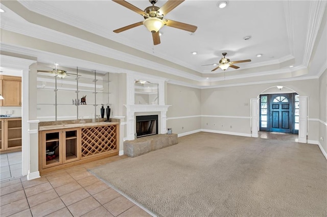 unfurnished living room with a raised ceiling, a tile fireplace, light tile patterned floors, and ornamental molding