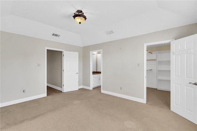 unfurnished bedroom featuring light carpet, ensuite bath, a spacious closet, a closet, and lofted ceiling