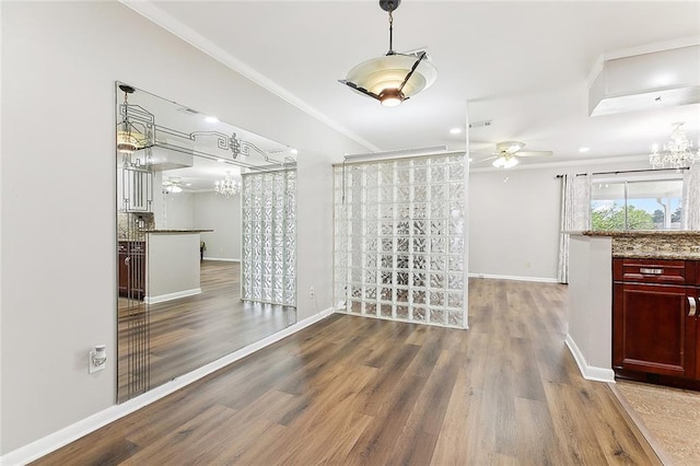 unfurnished dining area featuring crown molding, wood-type flooring, and ceiling fan with notable chandelier