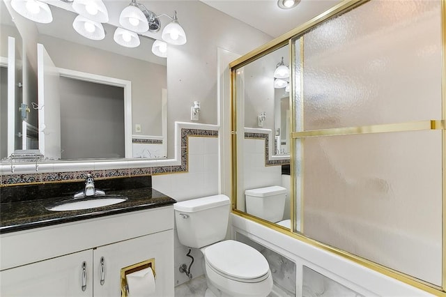 full bathroom featuring vanity, toilet, bath / shower combo with glass door, and tile walls