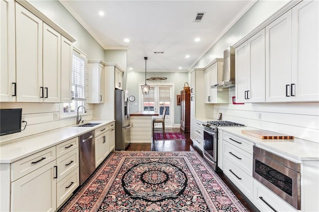 kitchen with sink, wall chimney exhaust hood, hanging light fixtures, dark wood-type flooring, and appliances with stainless steel finishes