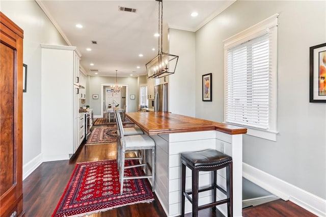 kitchen featuring a kitchen bar, stainless steel fridge, dark hardwood / wood-style flooring, ornamental molding, and white cabinets